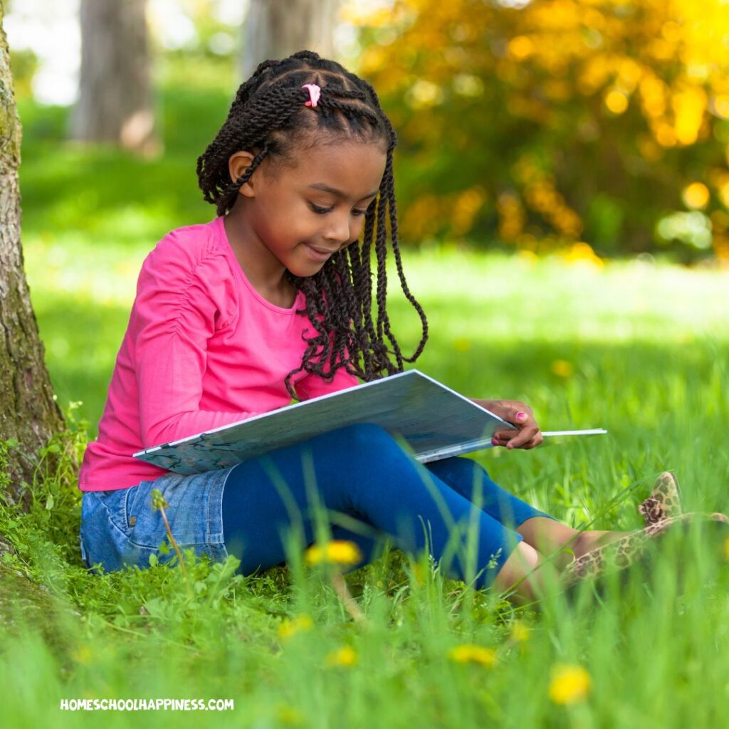 Girl reads a book on the grass, highlighting how summer reading supports visual and read/write learners.