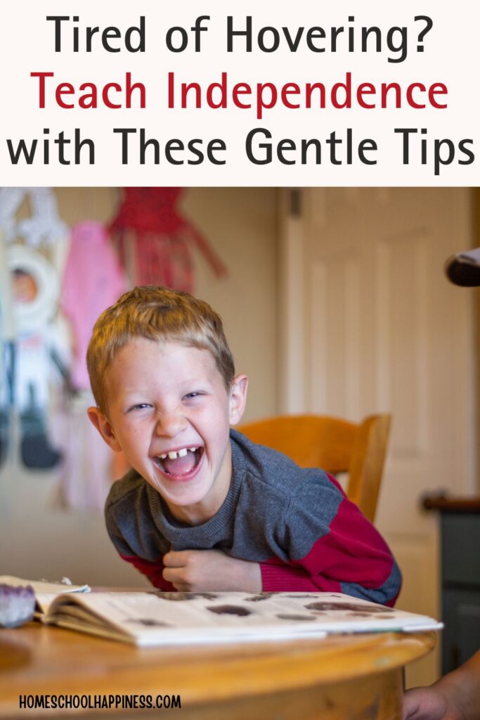 A young homeschool boy laughs joyfully while sitting at a table with an open book, representing the joy that can come from raising independent learners with gentle homeschool routines.